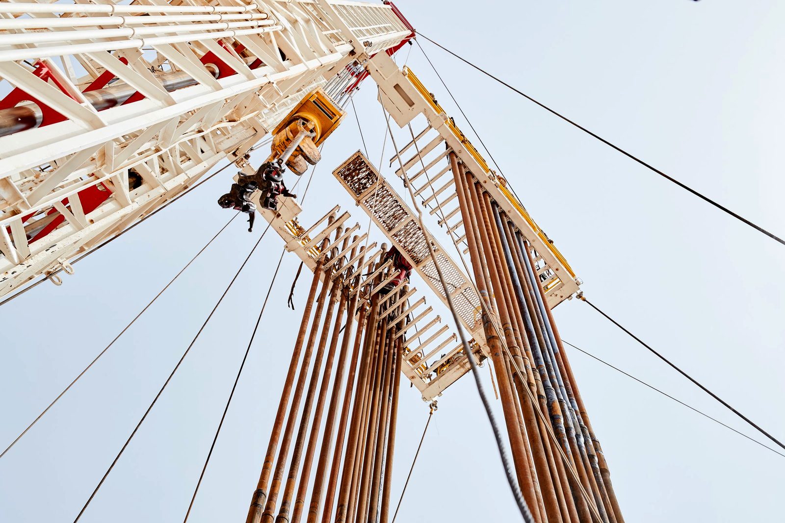 Rig mast in a refinery yard against a pale sky (licensed stock — not RANCO's own equipment)